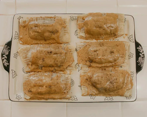Overhead shot of six chai almond butter pop tarts drizzled with icing in a decorative baking dish on a white tile surface. 
